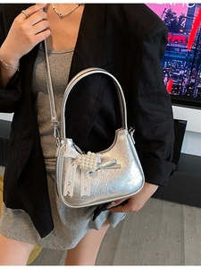 Silberne Metallic-Tasche mit Spitzenschleife und Perlenherz vor nächtlichem Stadthintergrund