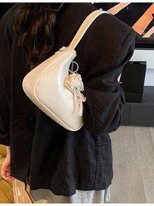 Schicke cremefarbene Dumpling-Bag mit Perlen-Spitzenschleife am schwarzen Blazer