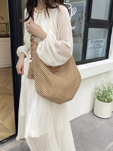 Straw hobo tote bag with leather straps and fringe detail worn by a model in sunlight
