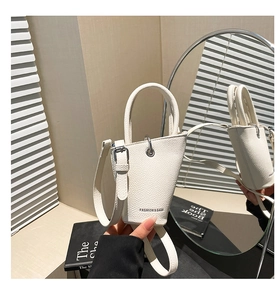 Détail du mini sac seau blanc avec poignées anneaux et texture cuir posé sur un livre