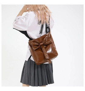 Detailansicht der glänzend braunen Ledertasche mit einer verzierten Nietenschleife