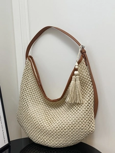 Woven straw hobo bag with brown leather shoulder strap and fringe detail on white background