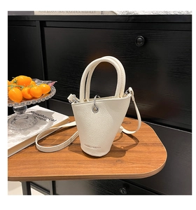Détail d'un sac seau en cuir grainé crème posé sur une surface en bois massif