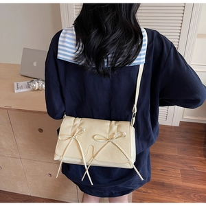 Détail du sac bandoulière crème avec nœuds décoratifs et fermeture à rabat chic