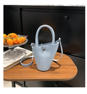 Détail du sac seau bleu clair en cuir texturé posé sur une table en bois naturel