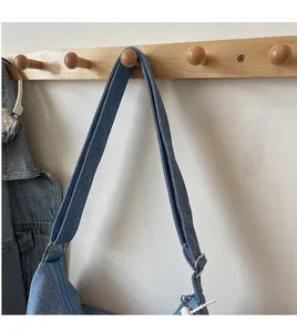 Detail of adjustable wide denim strap with silver metal buckle on blue canvas bag