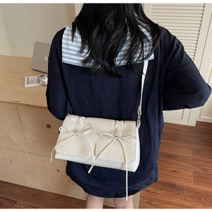 Sac bandoulière en similicuir crème avec nœud, porté par un mannequin en intérieur