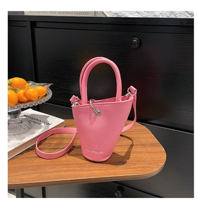 Gros plan du sac seau rose en cuir avec logo doré embossé sur une table en bois