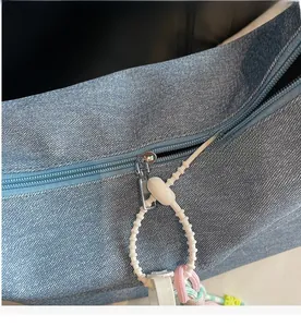 Detailed close-up of smooth silver zipper and colorful woven charm on blue denim handbag