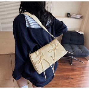 Détail du sac à bandoulière crème avec nœuds et texture en cuir plissé sur une chemise bleue
