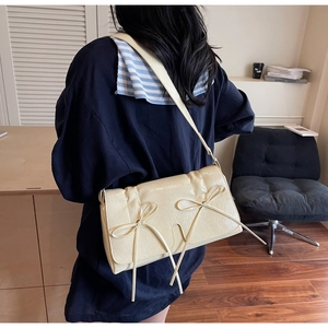 Détail du sac à bandoulière crème avec nœud et cuir plissé porté par un mannequin