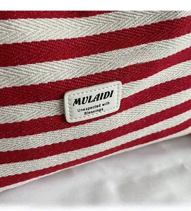Detailed close-up of red and white striped canvas bag with a leather brand logo patch