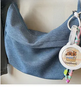 Close-up of blue denim half-moon shoulder bag with a cute white Capybara charm accessory