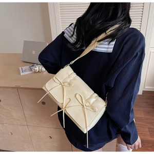 Détail d'un sac à bandoulière crème avec nœuds décoratifs et texture plissée élégante