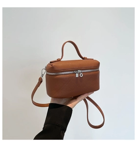 Detail view of brown pebble leather handbag with silver zippers and top handle