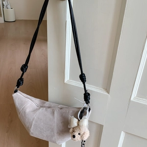 Détail du sac croissant en daim avec bandoulière à nœud et breloque ours en peluche