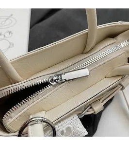 Detailed macro view of smooth silver metal zipper hardware on cream leather tote bag