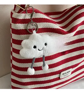 Close-up of white plush cloud charm with striped legs on a large striped tote bag