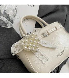 Detail of cream pleated patent leather bucket bag with pearl heart lace pendant