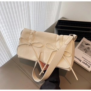 Détail du sac à bandoulière crème plissé avec nœuds décoratifs et finition brillante