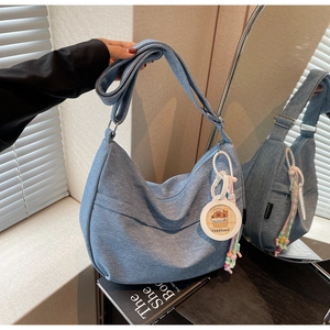 Detail of blue denim hobo bag featuring adjustable wide strap and capybara charm
