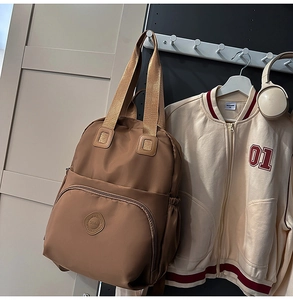 Detailansicht eines braunen Nylon-Rucksacks mit rundem Logo und großer Fronttasche