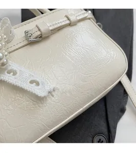 Detail of cream crossbody bag with pleated leather texture, pearl beads, and lace trim