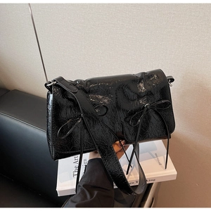 Vue détaillée d'un sac à bandoulière en cuir verni noir plissé orné de petits nœuds
