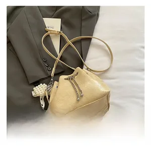 Detail der beige Beuteltasche mit Plissee-Textur, Perlenanhänger und Metallkettenzug