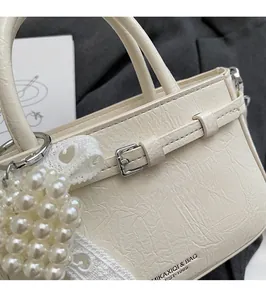 Detailed shot of beige tote bag with pearl lace charm and textured leather finish