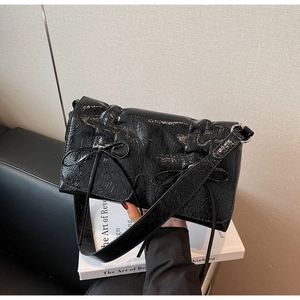 Détail d'un sac bandoulière noir brillant plissé avec de petits nœuds élégants