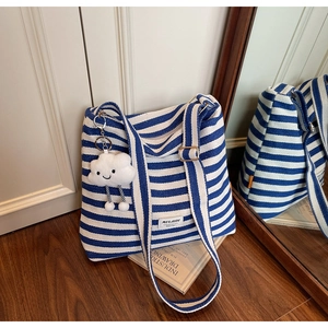 Detailed shot of striped canvas tote with adjustable strap and cloud plush pendant