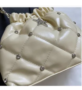 Détail d'un sac seau matelassé beige avec rivets en cristal et pendentif étoile