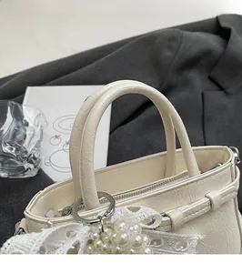 Close-up of cream tote bag with pearl lace pendant and textured faux leather finish