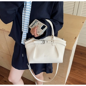 Detail of white lychee leather handbag featuring decorative metal buckle and detachable strap