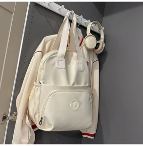 Detail eines cremefarbenen Rucksacks mit Front-Reißverschlusstasche und Logo-Emblem