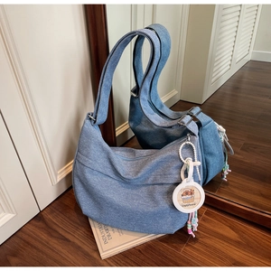 Detail of light blue denim crossbody bag featuring adjustable strap and capybara charm