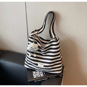 Detail shot of striped canvas tote bag with plush cloud charm on a black book