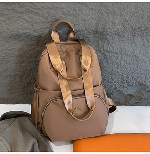 Detail eines hellbraunen Nylon-Rucksacks mit breiten Griffen und rundem Logo-Patch