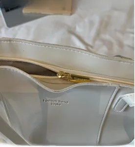 Close-up of smooth gold zipper closure on white leather tote bag with brand lettering