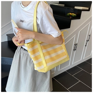 Detail of yellow and white striped mesh tote bag featuring premium leather handles and trim