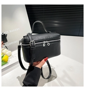 Detail of black lychee grain leather vanity bag with silver zippers and top handle