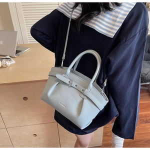 Detail of light blue textured leather handbag with buckle strap on a desk