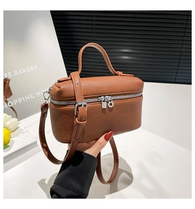 Detail view of brown pebbled leather texture and silver dual zipper on compact crossbody bag