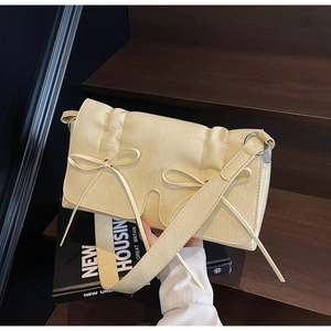 Détail du sac jaune crème en cuir plissé avec nœuds décoratifs sur fond de bois sombre