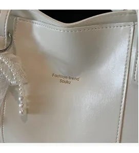 Close-up of white PU leather tote showing pebble texture and pearl lace charm
