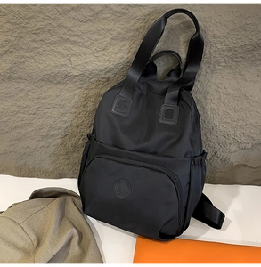 Detail eines schwarzen Nylon-Rucksacks mit rundem Logo-Aufnäher und Seitentasche