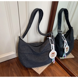 Detail of grey denim crescent bag with Capybara charm and wide adjustable shoulder strap