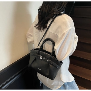 Detail of black lychee grain leather handbag with decorative buckle and metal eyelets