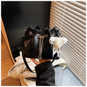 Detail of black glossy pleated bucket bag with metal chain drawstring and pearl bow charm